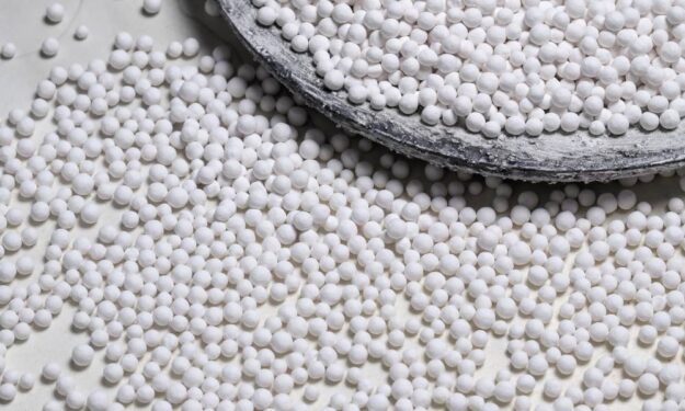 Dozens of small, round, white bead-like objects are on a desk. They are a type of nickel catalyst for chemical experiments.