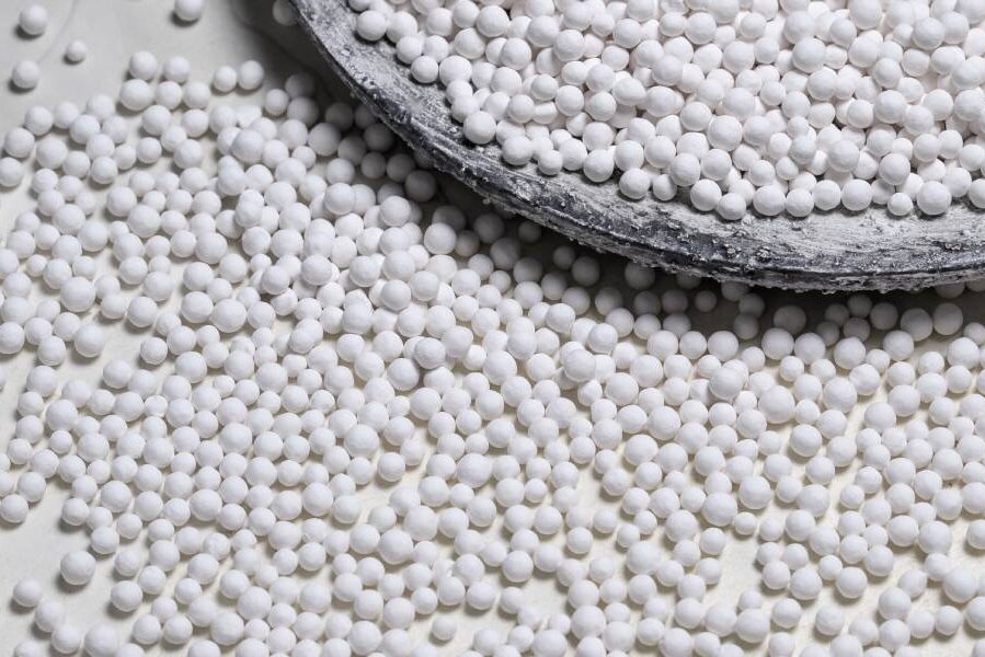 Dozens of small, round, white bead-like objects are on a desk. They are a type of nickel catalyst for chemical experiments.