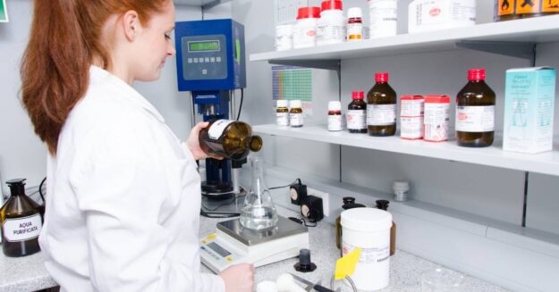 A young scientist at a work station. She's measuring and weighing a clear liquid inside of a flask.