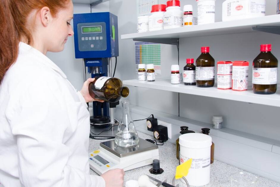 A young scientist at a work station. She's measuring and weighing a clear liquid inside of a flask.