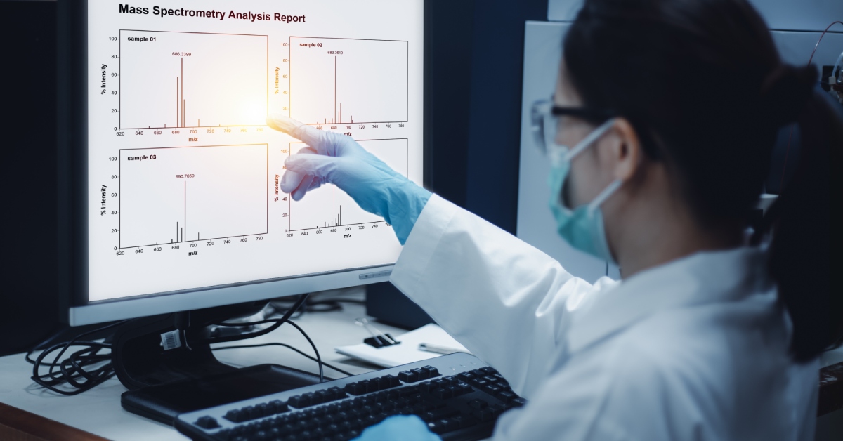 A woman in a lab coat and mask is monitoring a screen with several graphs on it. The screen reads "Mass Spectrometry Analysis Report"
