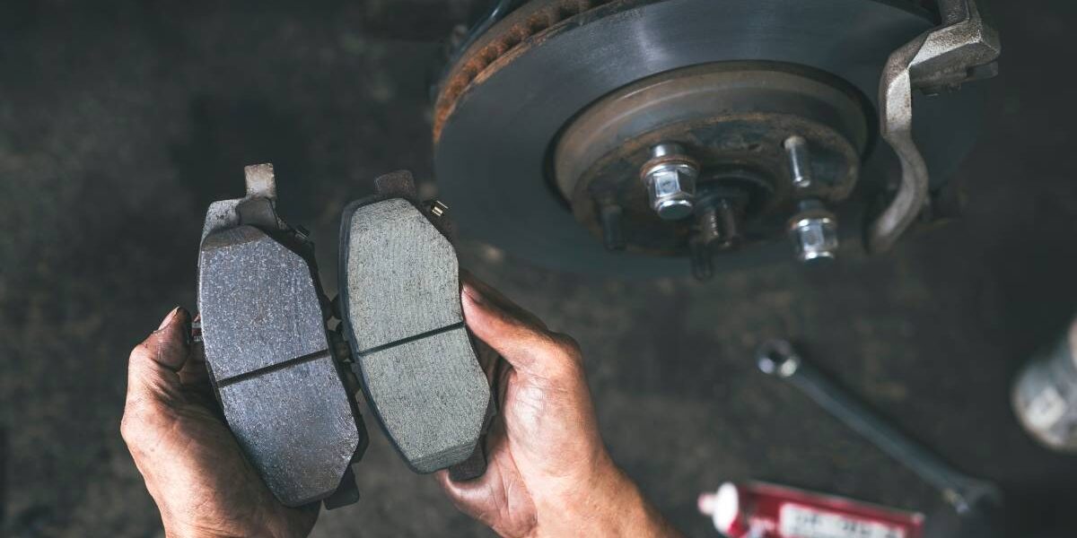 A person holding the brake pads of a car. One pad is smooth, while the other has grooves and is darker in color.