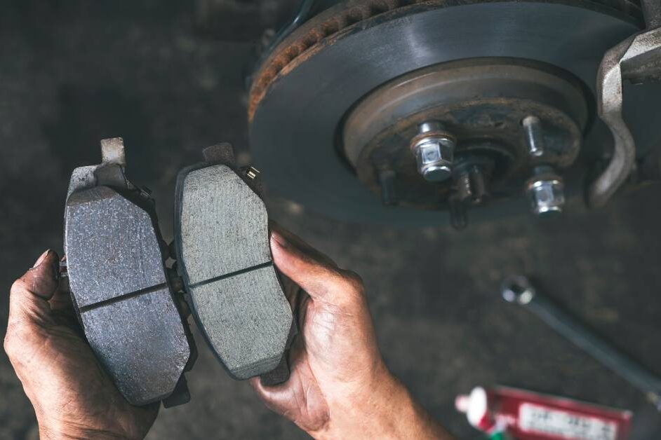 A person holding the brake pads of a car. One pad is smooth, while the other has grooves and is darker in color.