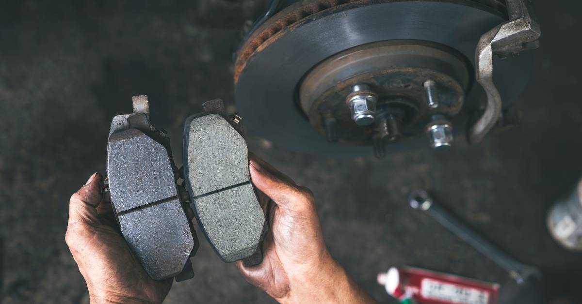 A person holding the brake pads of a car. One pad is smooth, while the other has grooves and is darker in color.