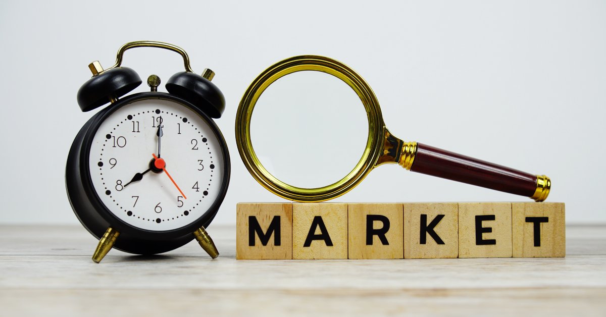Wooden tiles lined up with letters that spell MARKET with a magnifying glass placed on top and an alarm clock nearby.
