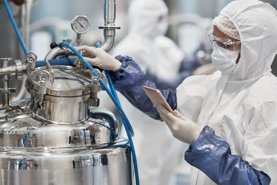 An individual wearing a white protective suit, goggles, and gloves while operating chemical equipment.