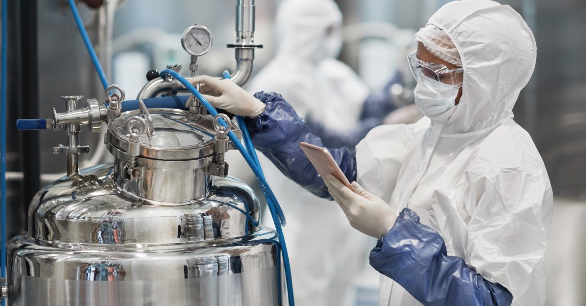 An individual wearing a white protective suit, goggles, and gloves while operating chemical equipment.