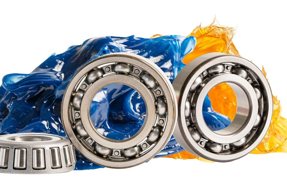 Stainless steel ball bearings in front of blue and orange lithium grease, against a white background.
