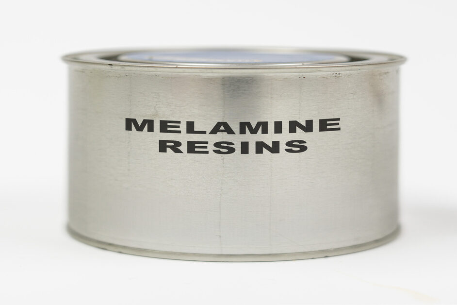 A metal container labeled "Melamine Resins" in black letters. The container sits against a plain white background.