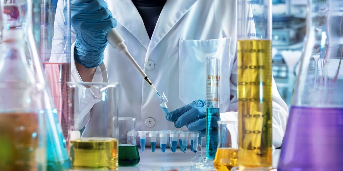 4 Types of Chemicals That Act as Stain Repellents A scientist in a lab coat and gloves uses a micropipette to transfer blue liquid into a test tube on a busy lab bench.