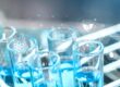 A close-up of test tubes with blue chemicals in a research lab, overlaid with digital icons symbolizing DNA, atoms, and data.