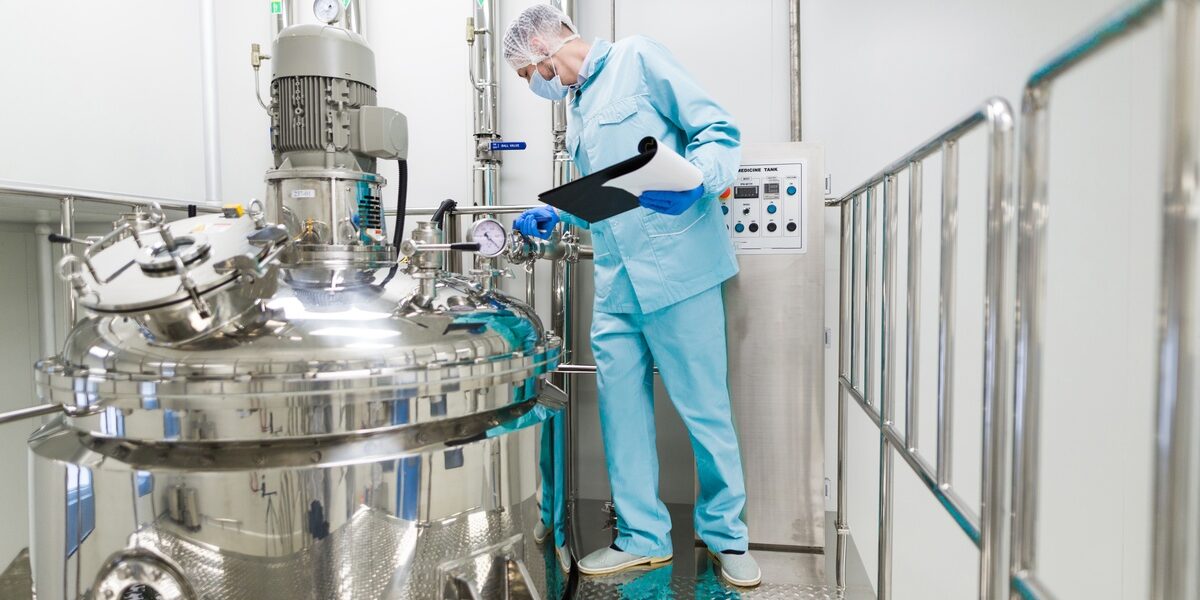A technician inspects gauges on a stainless-steel chemical reactor inside a controlled industrial processing facility.