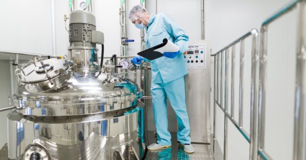 A technician inspects gauges on a stainless-steel chemical reactor inside a controlled industrial processing facility.