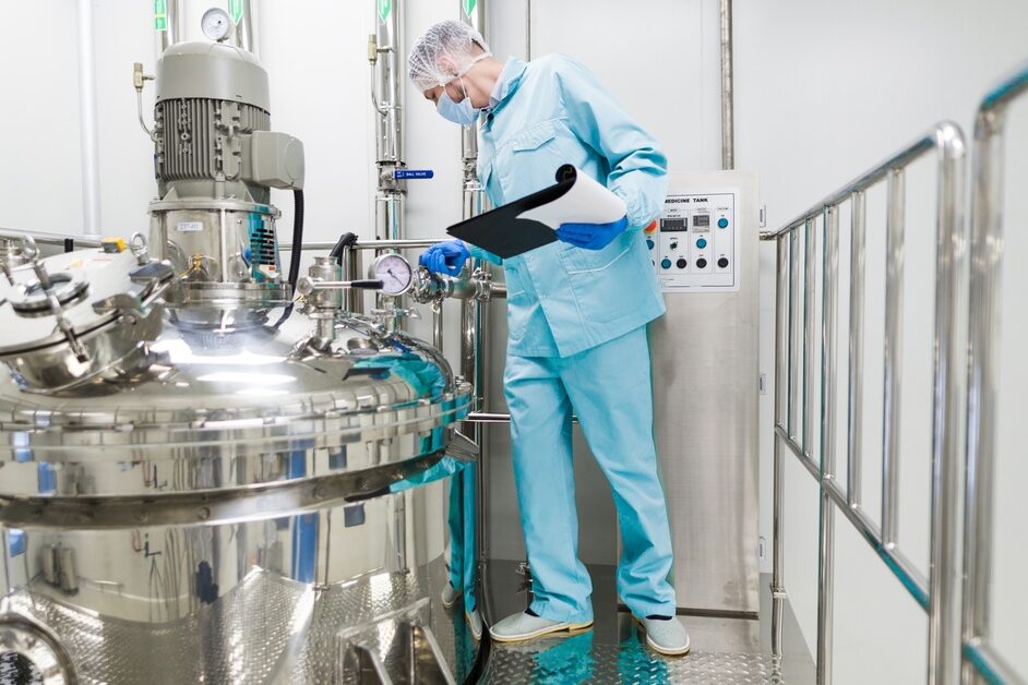 A technician inspects gauges on a stainless-steel chemical reactor inside a controlled industrial processing facility.