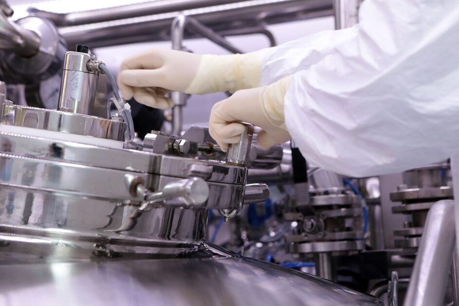 A technician in white protective clothing and gloves adjusts equipment on stainless-steel manufacturing machinery.
