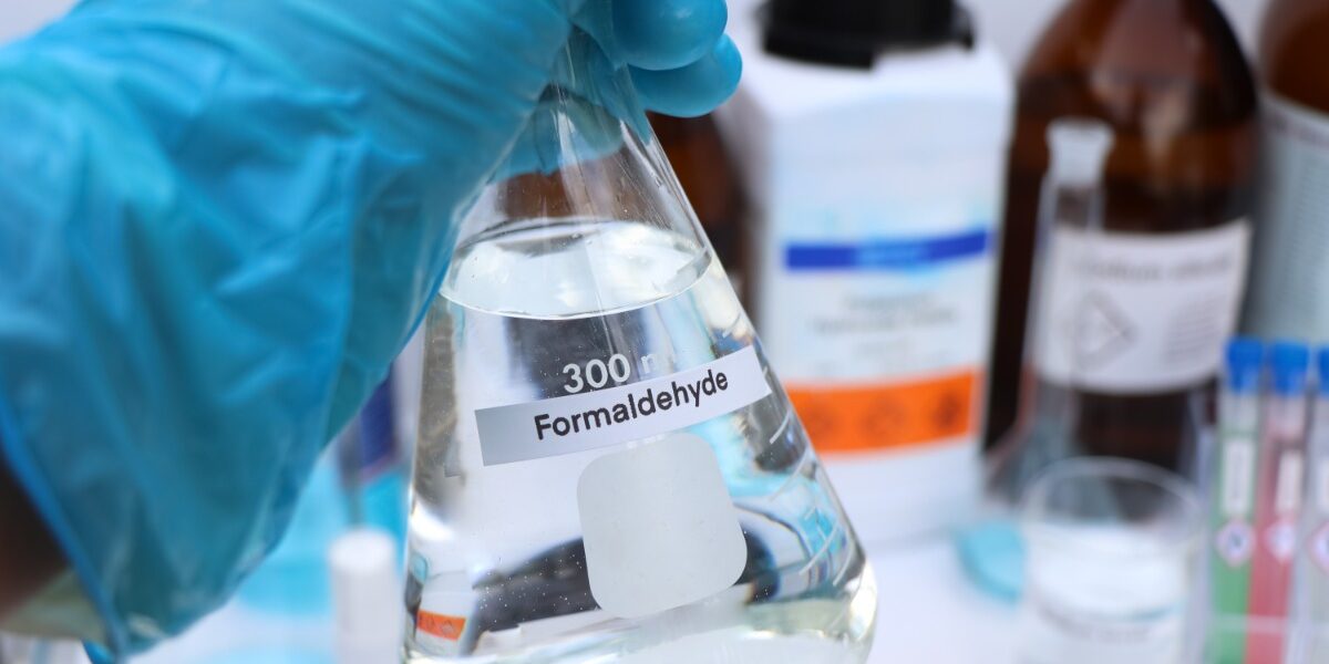 A person who is wearing a glove on their hand is holding a beaker filled with a clear liquid.