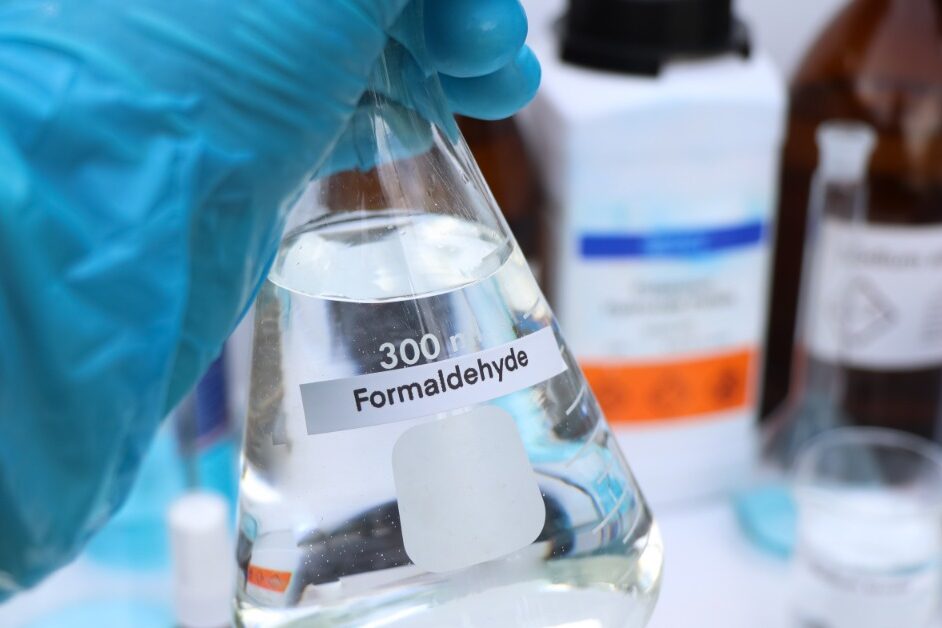 A person who is wearing a glove on their hand is holding a beaker filled with a clear liquid.
