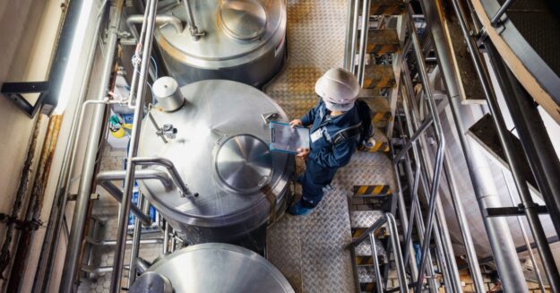 A person in a blue jumpsuit is standing over a metal container. There are other containers on either side of the first.