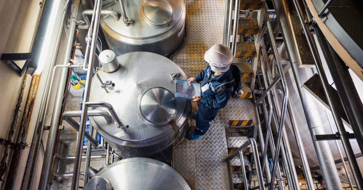 A person in a blue jumpsuit is standing over a metal container. There are other containers on either side of the first.