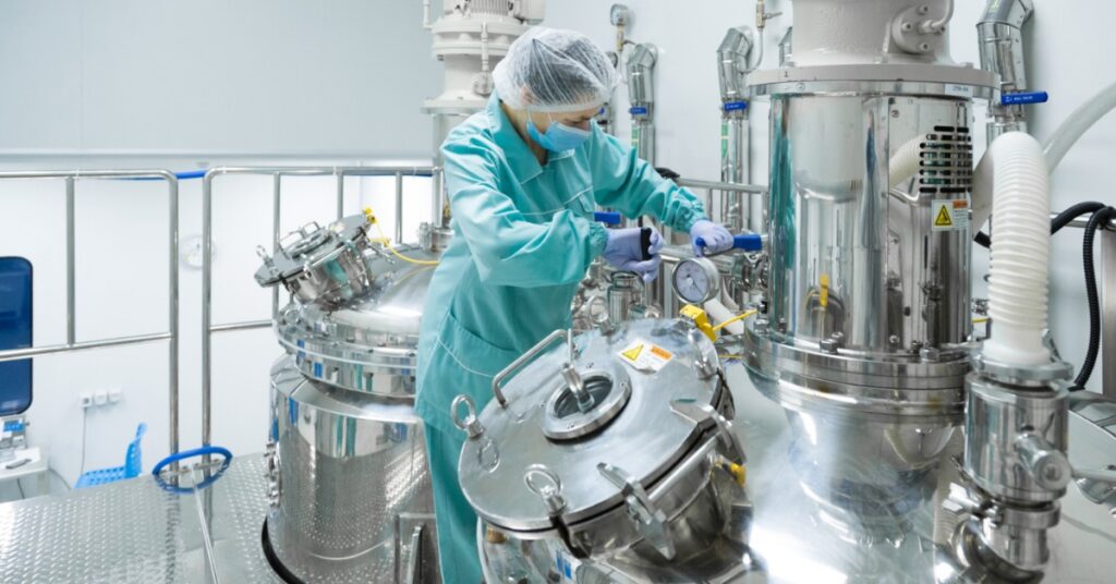 A woman in teal scrubs is working on a machine. There is a second machine behind her.