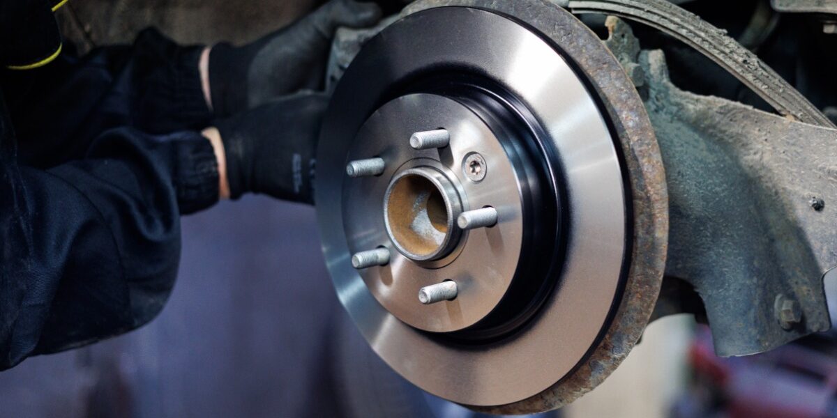 A person is reaching into the undercarriage of a car. The tire is off the vehicle and you can see the rotor. A person is reaching into the undercarriage of a car. The tire is off the vehicle and you can see the rotor.