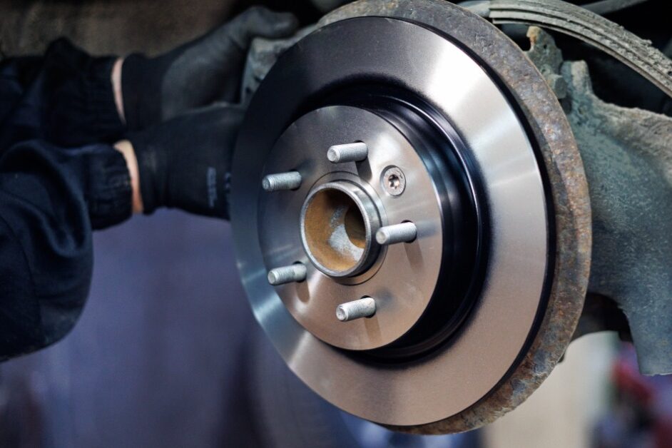 A person is reaching into the undercarriage of a car. The tire is off the vehicle and you can see the rotor.