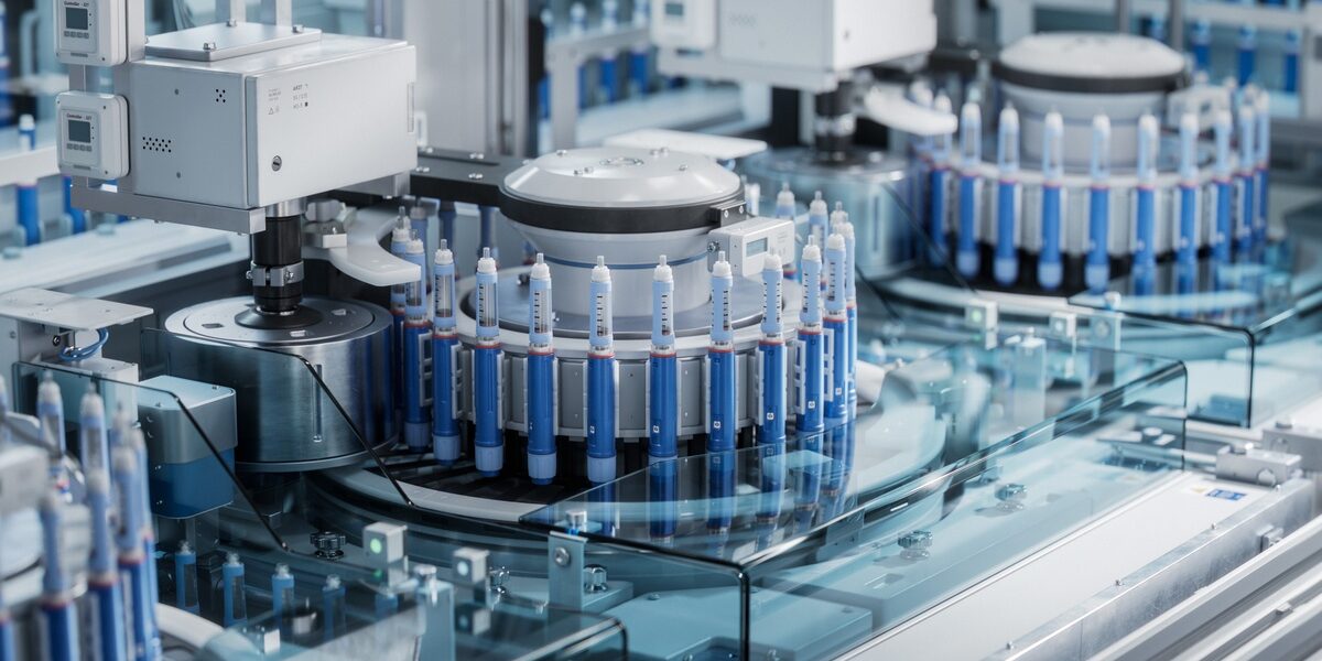 A piece of machinery has a number of capsules in a circle. There is another similar machine in the background.