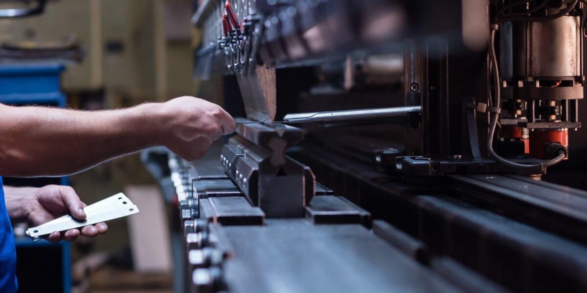 A man in a blue shirt is gripping onto a handle that is attached to some type of manufacturing machine.