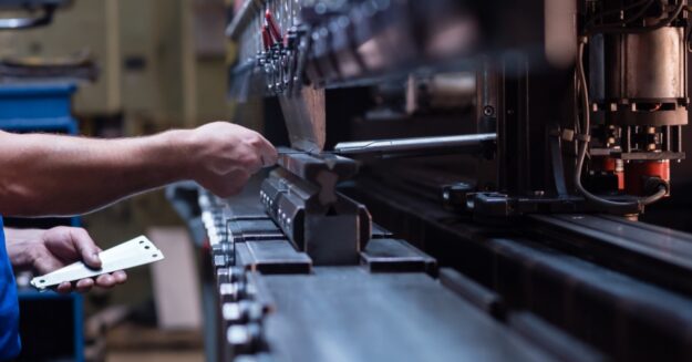 A man in a blue shirt is gripping onto a handle that is attached to some type of manufacturing machine.