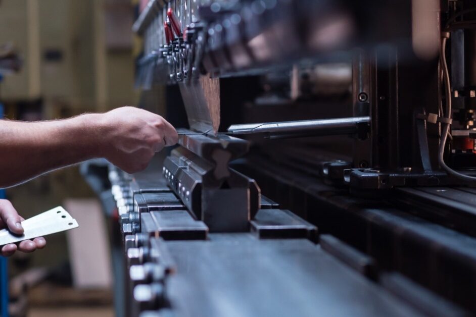 A man in a blue shirt is gripping onto a handle that is attached to some type of manufacturing machine.