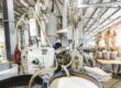 An industrial machine has several tubes coming out of it. Some of those tubes are going into barrels filled with white stuff.