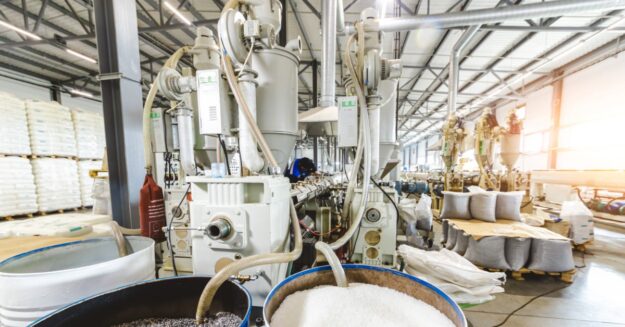 An industrial machine has several tubes coming out of it. Some of those tubes are going into barrels filled with white stuff.