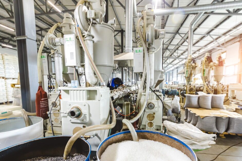 An industrial machine has several tubes coming out of it. Some of those tubes are going into barrels filled with white stuff.