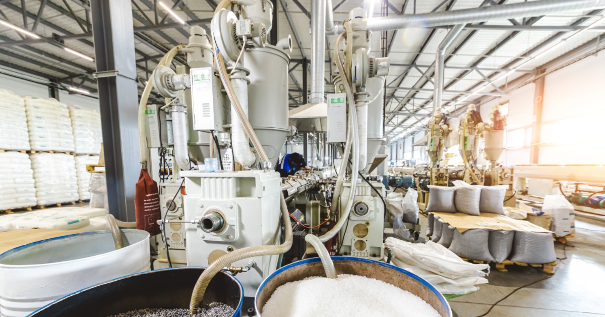 An industrial machine has several tubes coming out of it. Some of those tubes are going into barrels filled with white stuff.