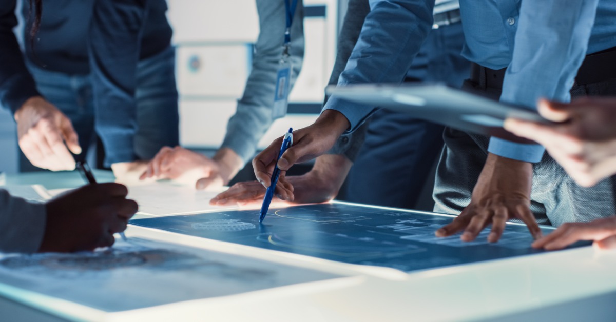 Several people are gathered around a table. There is a blue document on the table that everyone is looking at.