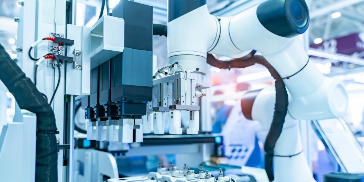 A robotic arm is reaching for a vial. The arm is in a sterile, industrial environment. There are red wires.