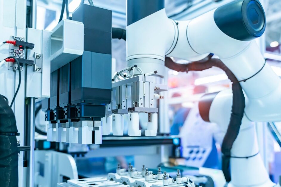 A robotic arm is reaching for a vial. The arm is in a sterile, industrial environment. There are red wires.
