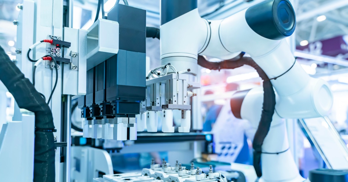 A robotic arm is reaching for a vial. The arm is in a sterile, industrial environment. There are red wires.