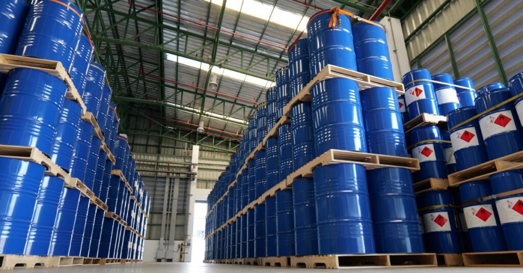 A warehouse is filled with pallets of blue barrels. The barrels are all on pallets and stacked on top of one another.