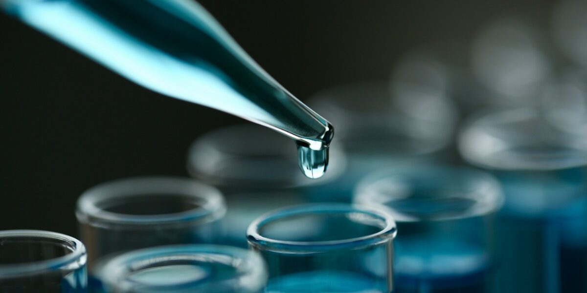 A dropper is dropping a blue liquid into a clear test tube that already has blue liquid in it.