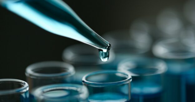 A dropper is dropping a blue liquid into a clear test tube that already has blue liquid in it.