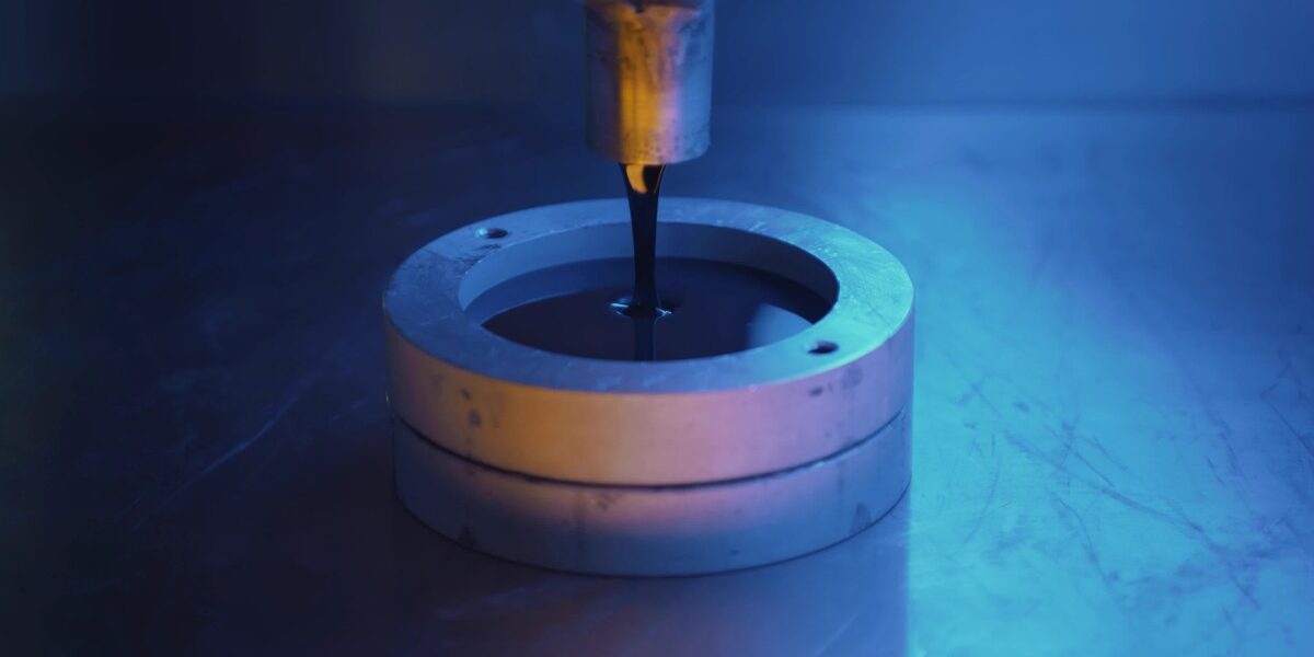 Resin is being poured into a mold. The mold is in an industrial setting and there is a dark blue light.